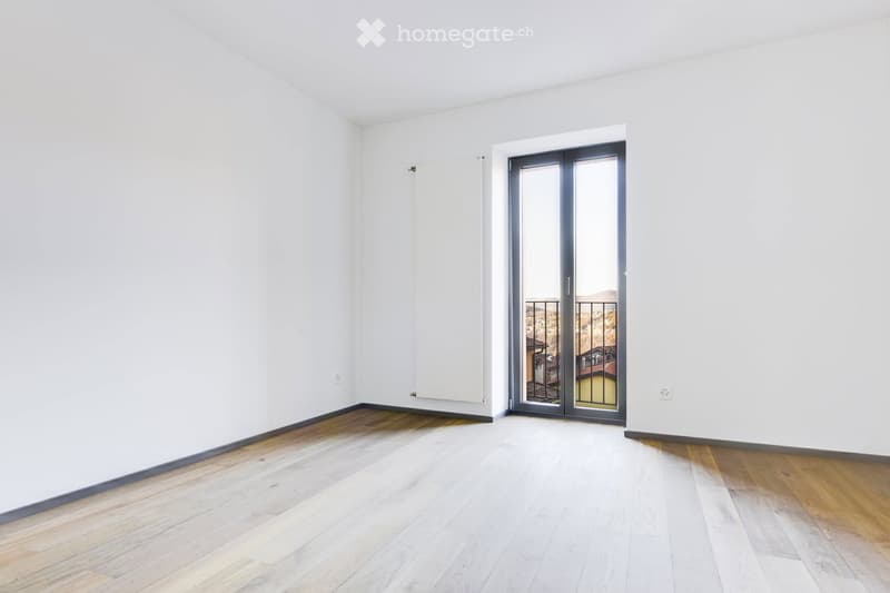 Empty room with white walls, wooden flooring, and a large sliding glass door leading to a balcony.