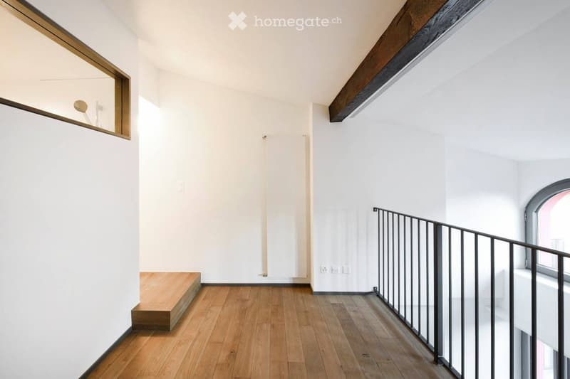 Bright, minimalist hallway with wooden flooring, white walls, and a modern black metal railing leading to an upper level.