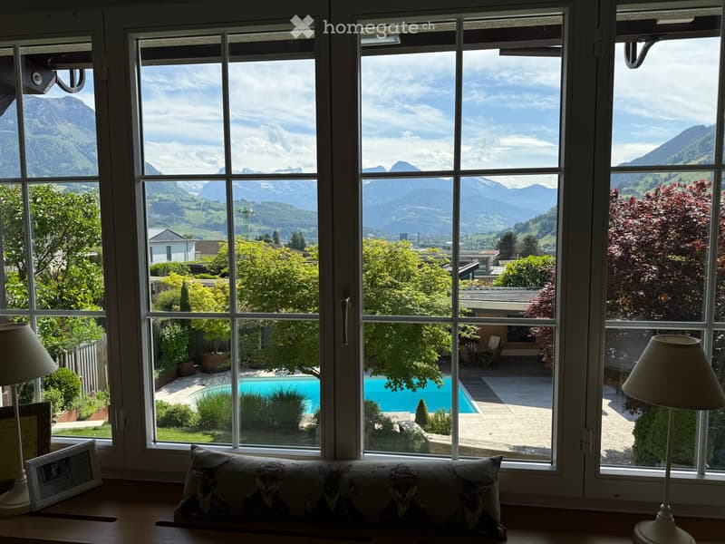 Bright room with large windows offering a scenic mountain view and a swimming pool in the garden.