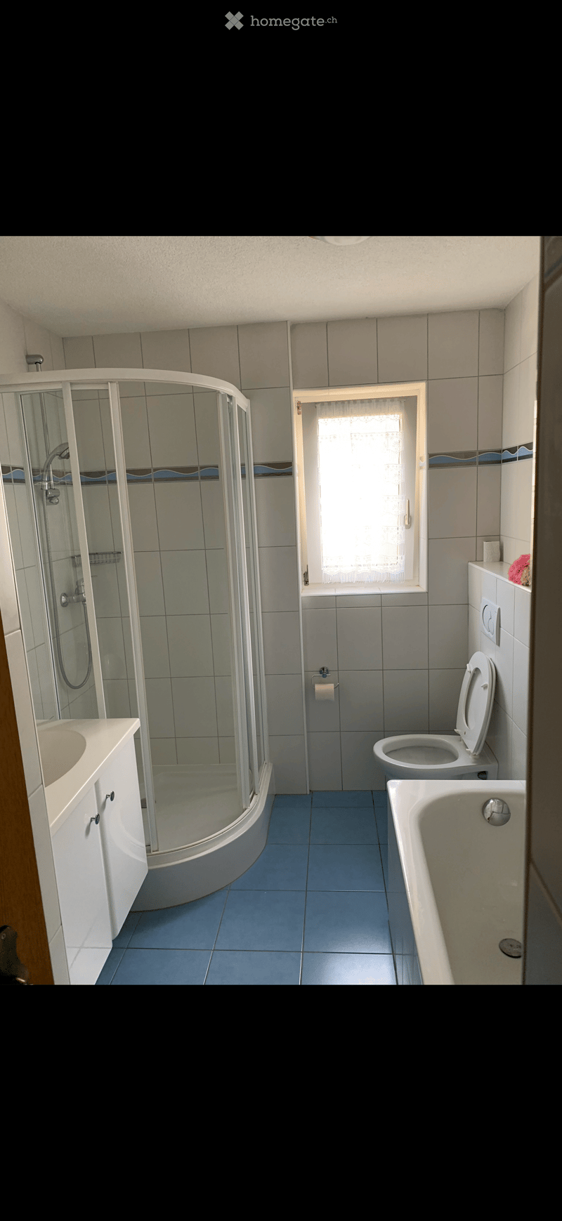 Bathroom with blue tiled floor, white tiled walls, a corner shower with glass enclosure, a sink with cabinet, a toilet, and a bathtub.