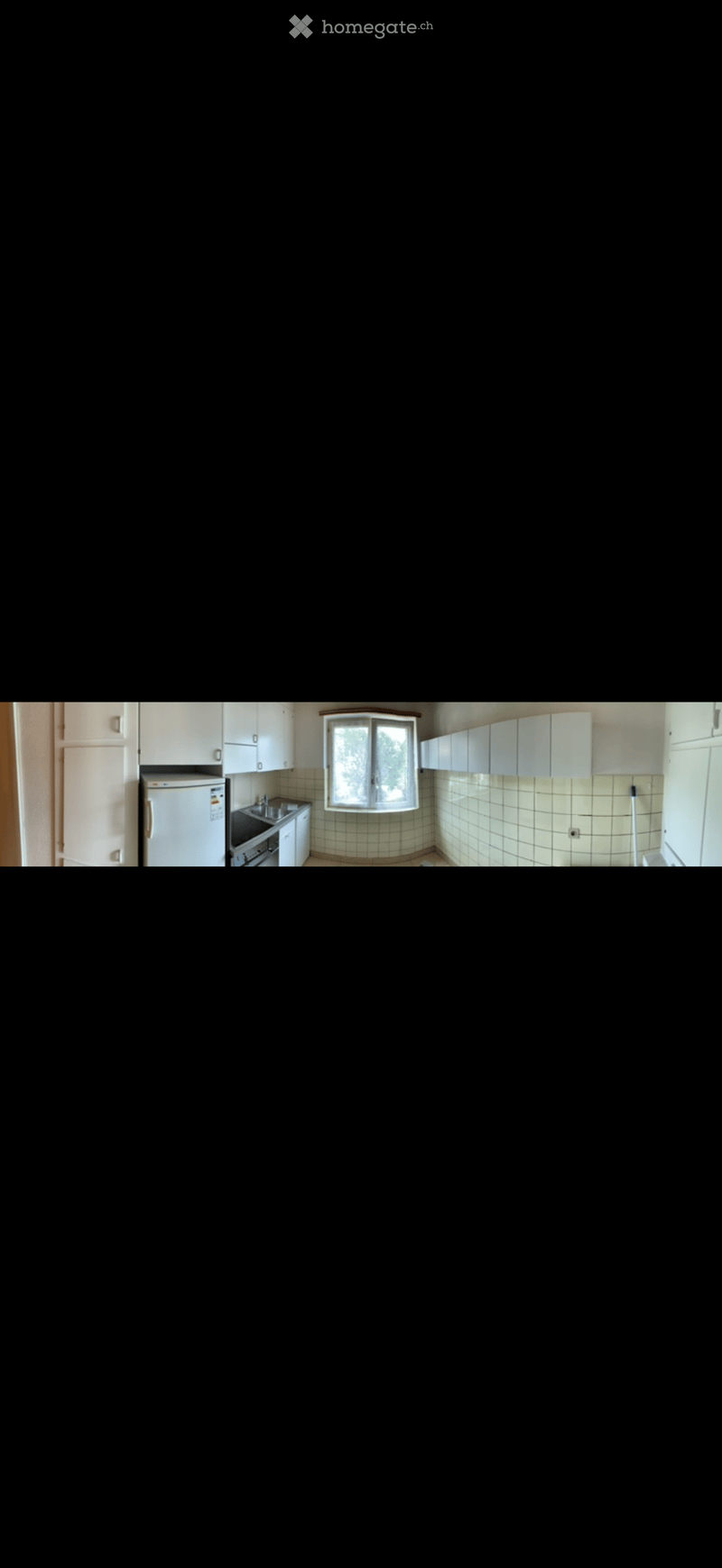 A small kitchen with white cabinets, a refrigerator, a sink, and a stove. The walls are tiled in a light green pattern, and there is a window above the sink.