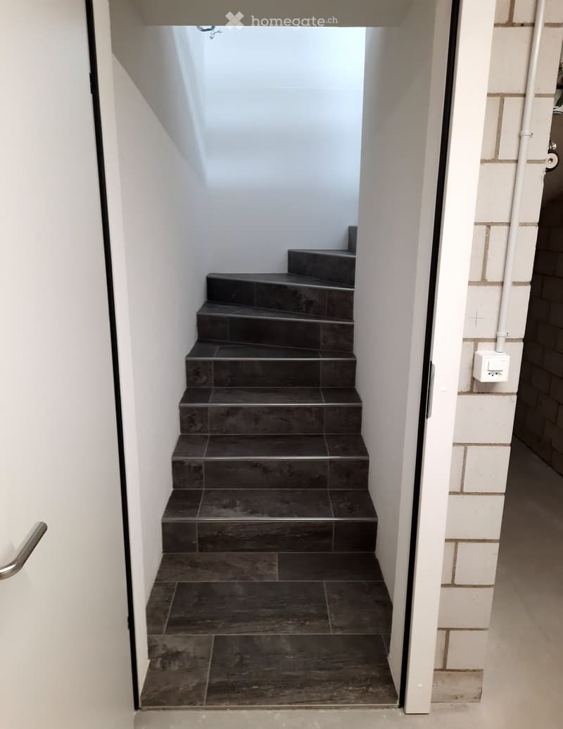 Staircase with tiled steps, white walls, and a white door