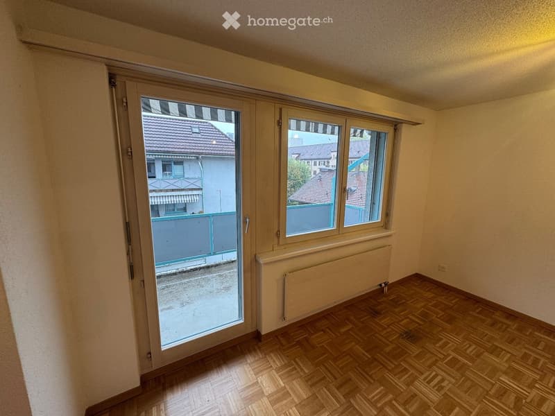 Empty room with wooden flooring, large window, and sliding glass door leading to a balcony.