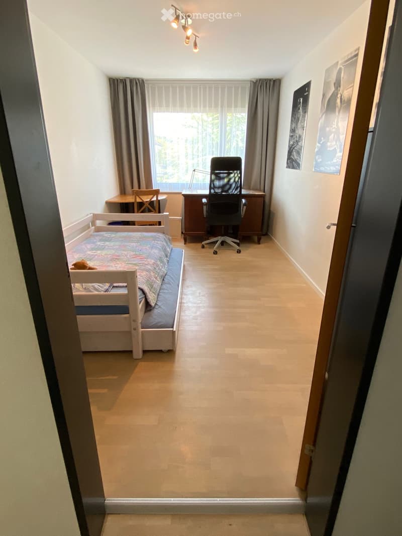 Cozy bedroom with a single bed, desk, office chair, and small table near the window with curtains.