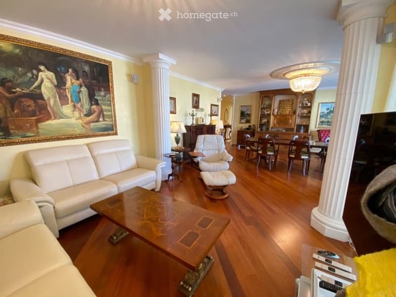 Elegant living room with hardwood flooring, white leather sofa, coffee table, armchair, dining area with table and chairs, decorative lamps, and artwork on the walls.