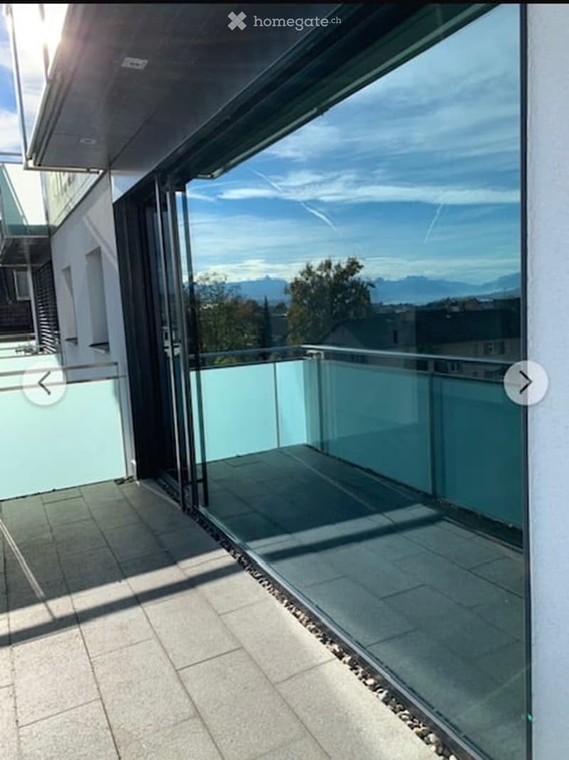 Modern balcony with large glass sliding doors, light-colored tiles, and a clear view of the surrounding landscape and mountains.