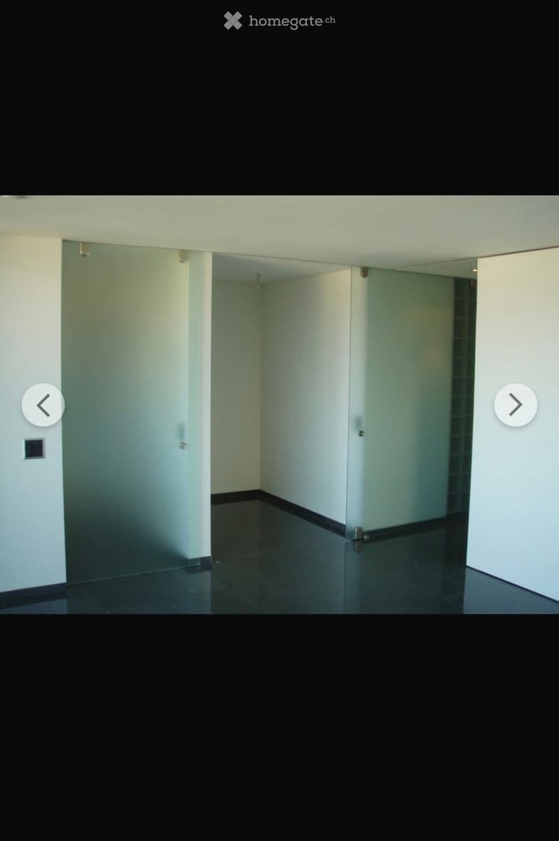 Empty room with white walls, dark tiled floor, and a single door leading to another space.