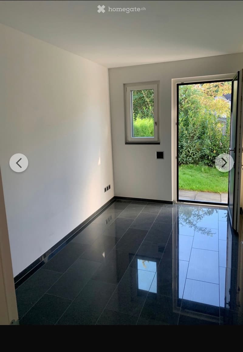 Empty hallway with dark tiled flooring, white walls, and two windows, one of which is open to a garden view.