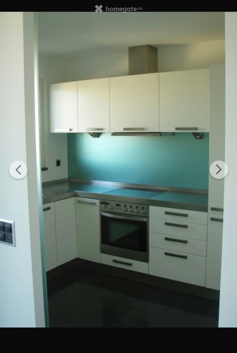 Modern kitchen with white cabinets, stainless steel oven, and dark tiled floor.