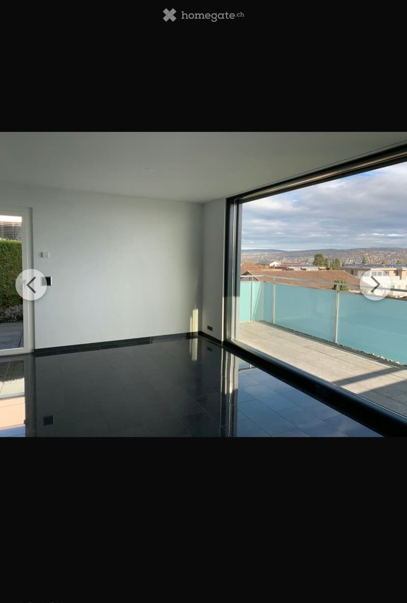 Empty room with dark tiled floor, white walls, large window with a view of the city and a balcony area with a glass railing.