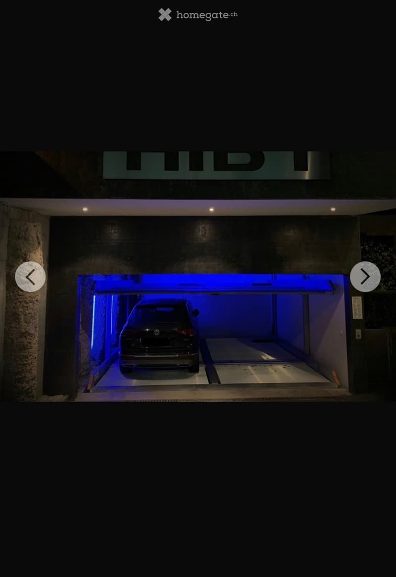 Underground parking area with a single car parked inside, illuminated by blue lighting.