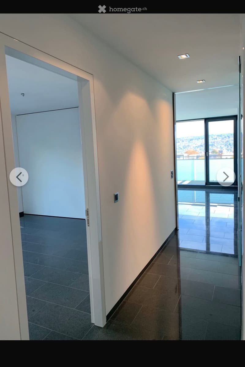 Empty hallway with tiled floors, white walls, and recessed lighting. Features a glass door leading to a balcony or outdoor area.