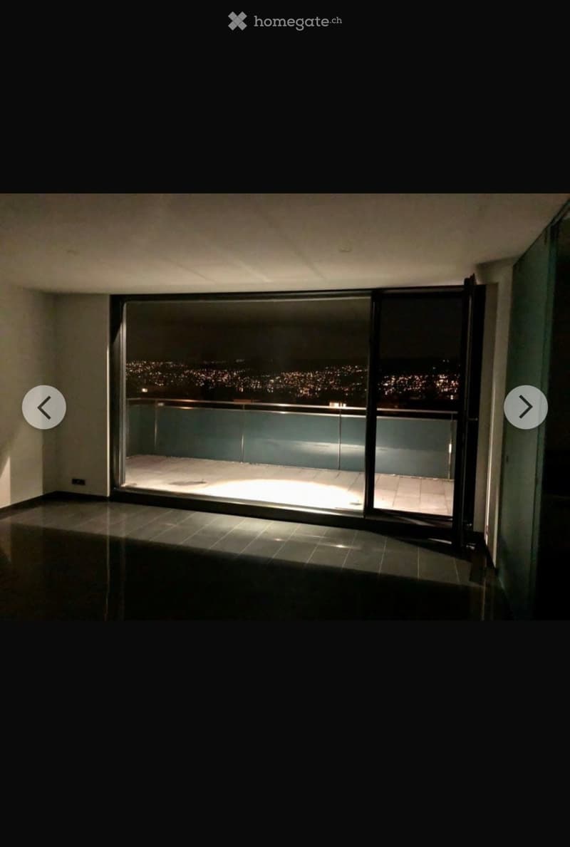 Large balcony with glass walls, overlooking a cityscape at night, illuminated tiles, and a railing.