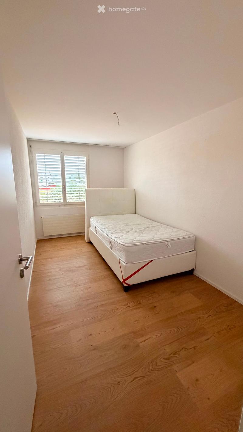 A small, unfurnished bedroom with a single bed, wooden flooring, and a window with blinds.