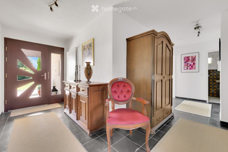 Elegant hallway with a red upholstered chair, wooden cabinet, vase on top, and artwork on the walls.