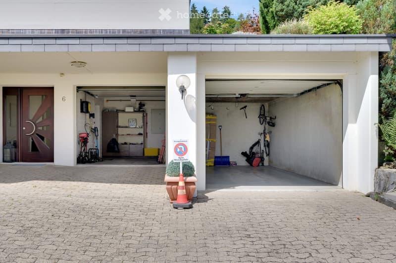Two-car garage with a covered entrance, bicycles, and storage items inside. The entrance features a decorative door with the number 6, and there is a sign indicating no parking.