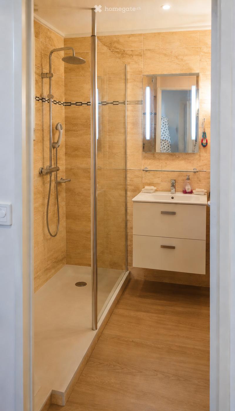 Modern bathroom with a glass-enclosed shower, a sleek sink with a modern faucet, and a large mirror above it. The walls are tiled in a warm, light wood tone, and the floor is made of light wood.