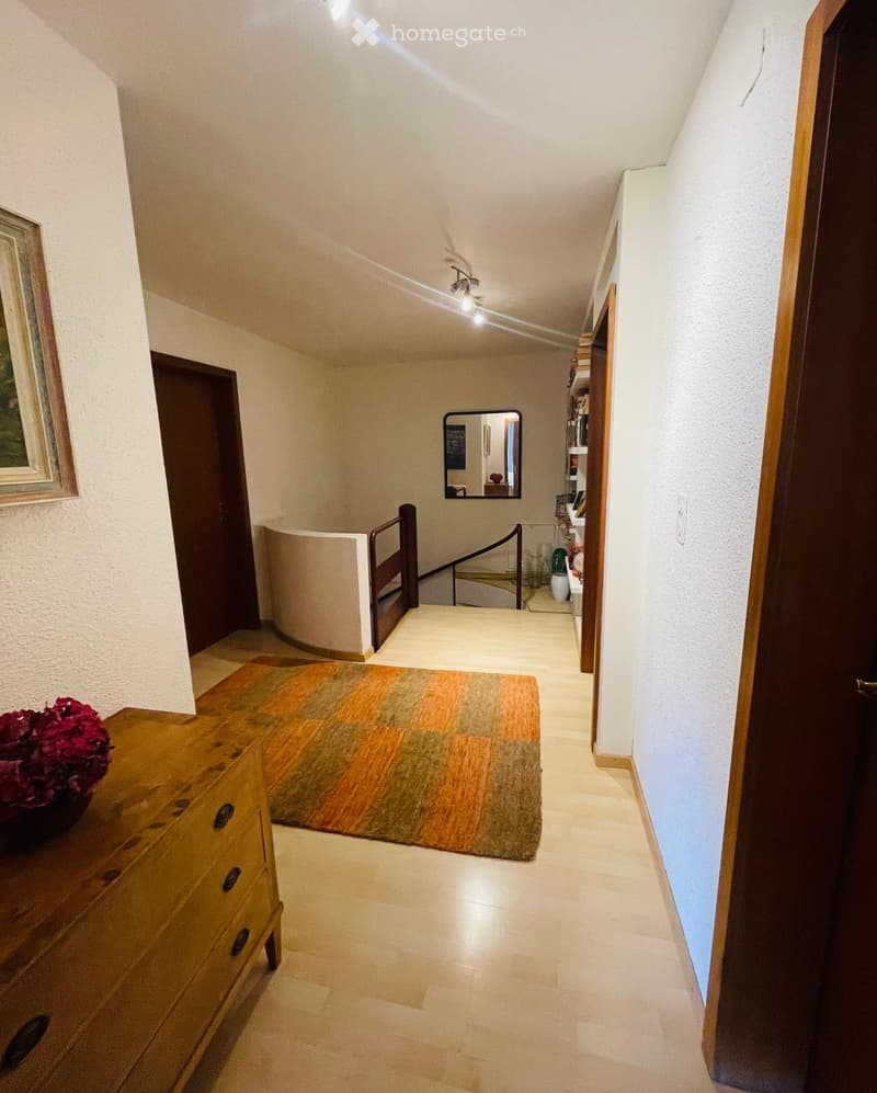Hallway with beige tiled flooring, wooden dresser with drawers, colorful rug, and a mirror on the wall.