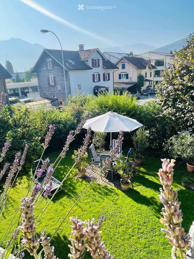 A well-maintained garden with green grass, lavender plants, and a seating area featuring a table, chairs, and an umbrella.