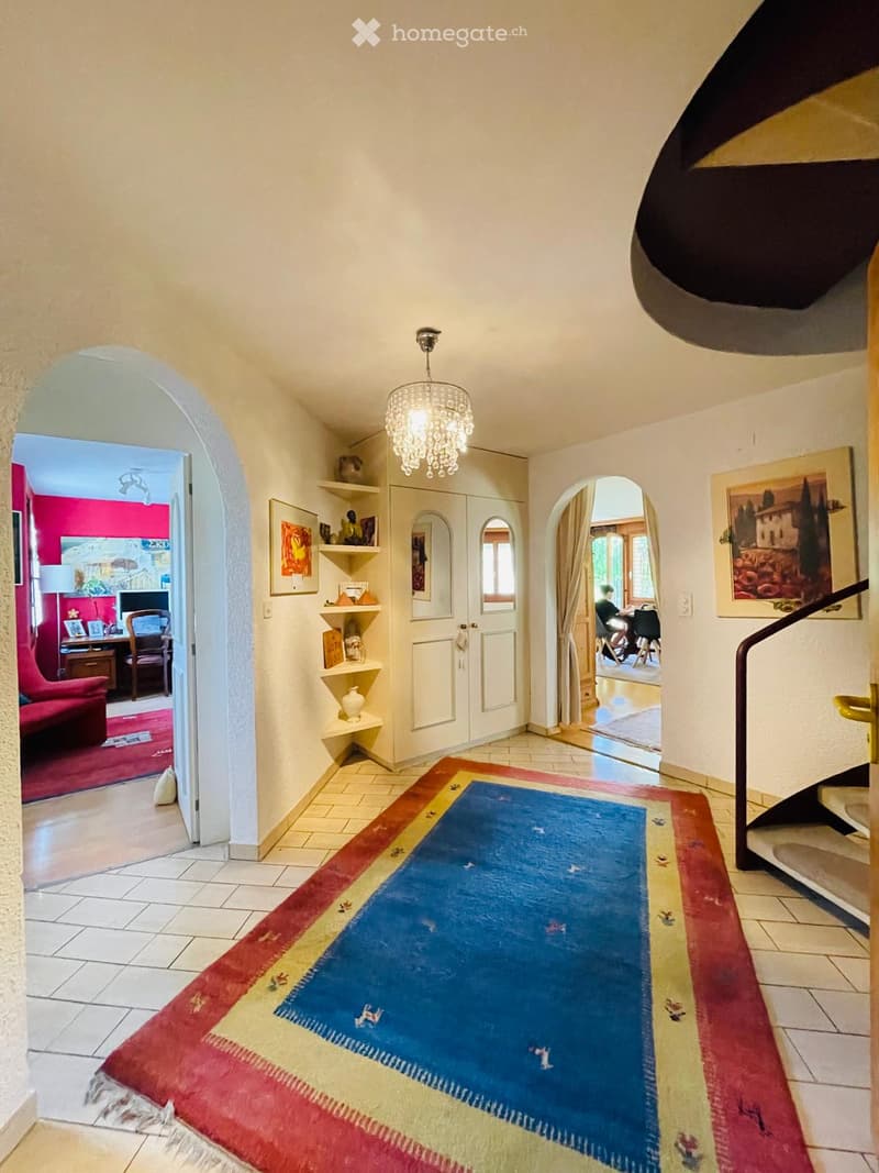 Elegant hallway with a colorful runner rug, white walls, arched doorways leading to different rooms, and a chandelier hanging from the ceiling.
