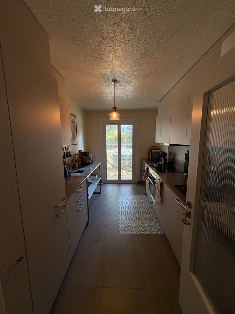 Modern kitchen with white cabinets, stainless steel appliances, a small rug, and a sliding glass door leading to an outdoor area.