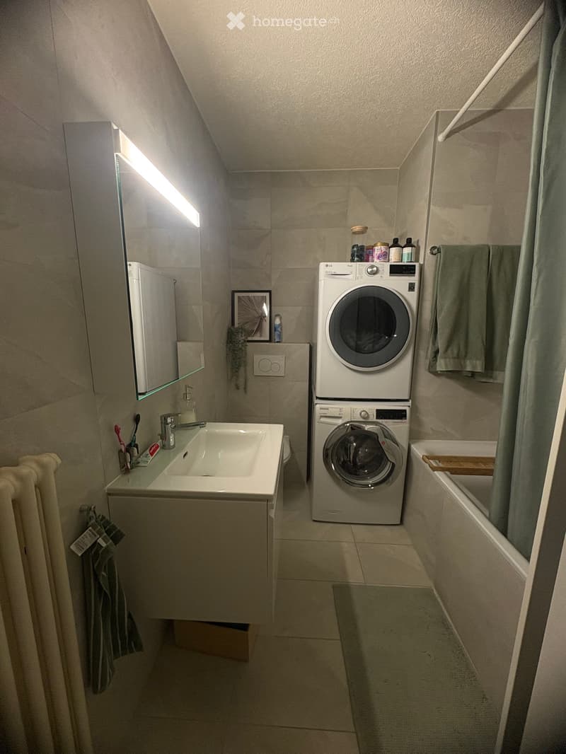 Compact bathroom with a sink, washing machine, and bathtub. Includes a mirror, towels, and personal care items.