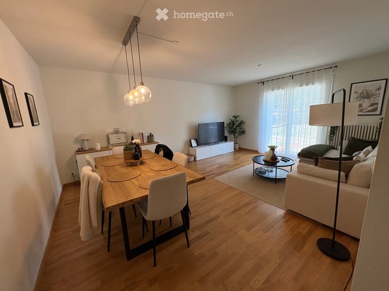 Open-plan living and dining area with wooden flooring, a sofa, dining table with chairs, a TV, and decorative items.
