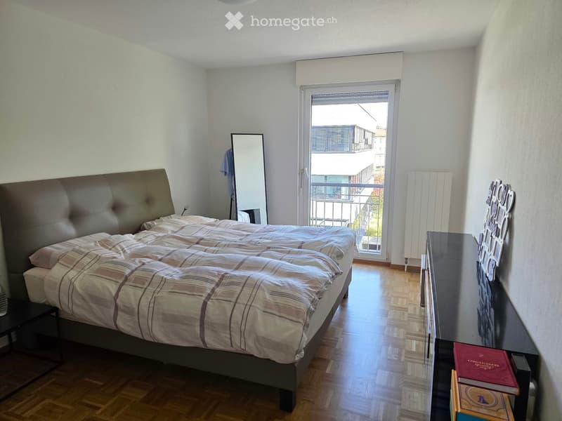 Bright bedroom with a large bed, nightstand, mirror, radiator, and a balcony view.