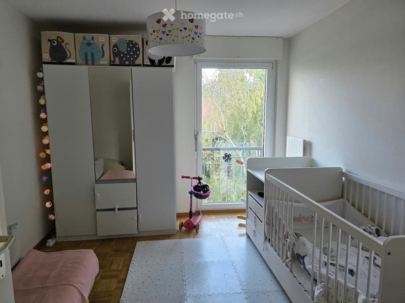 Brightly lit children's bedroom with a crib, wardrobe, scooter, and decorative lamp.