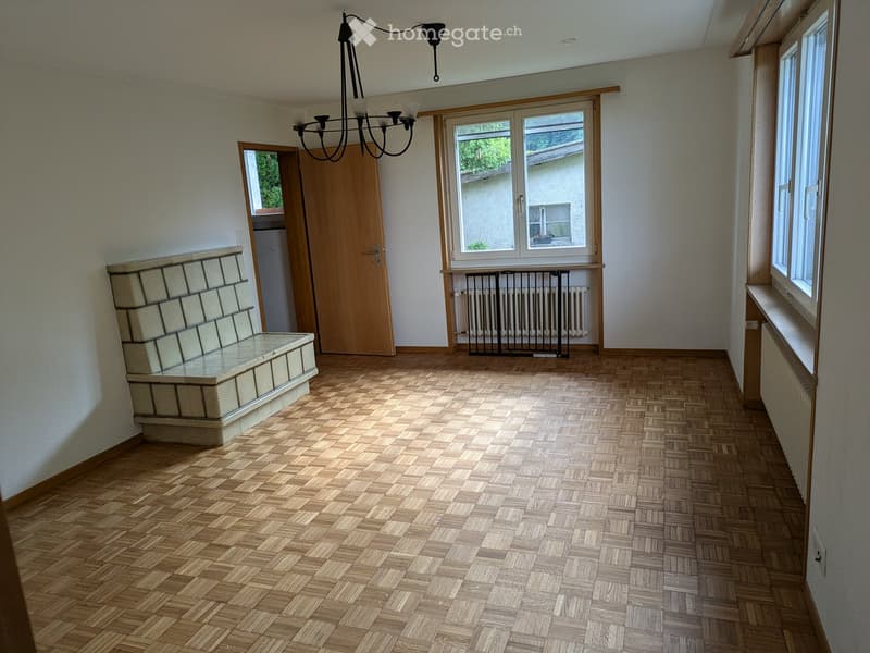 Empty room with wooden herringbone flooring, white walls, large windows, a wooden door, and a built-in bench with a glass top.