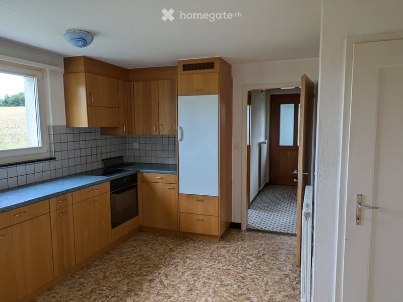 The kitchen features wooden cabinets, a refrigerator, an oven, and a countertop. The floor is tiled, and there is a window on the left side.