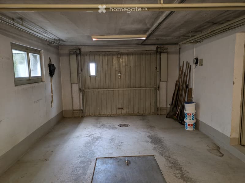 Empty room with concrete floor, wooden door, windows, and some tools and buckets in the corner.