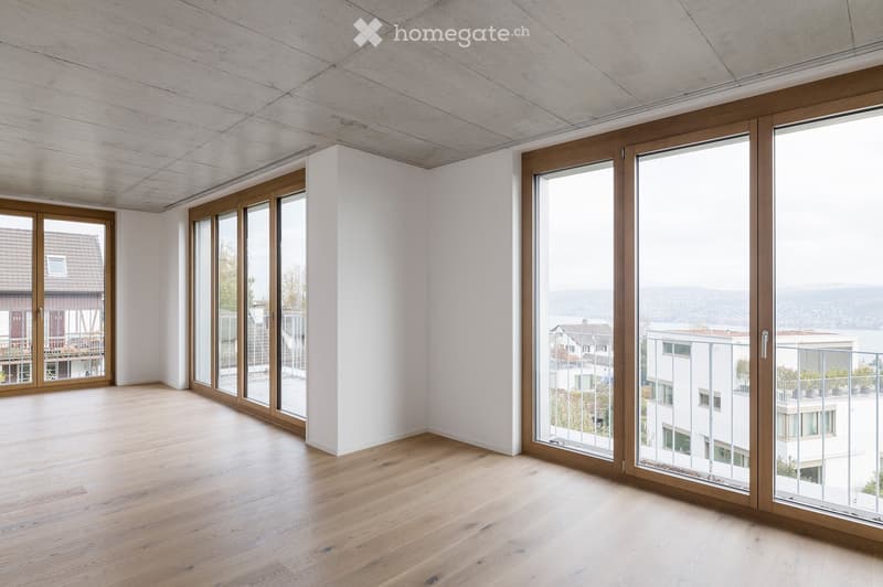 Empty room with light wooden flooring, white walls, and large sliding glass doors offering a view of the surrounding area.