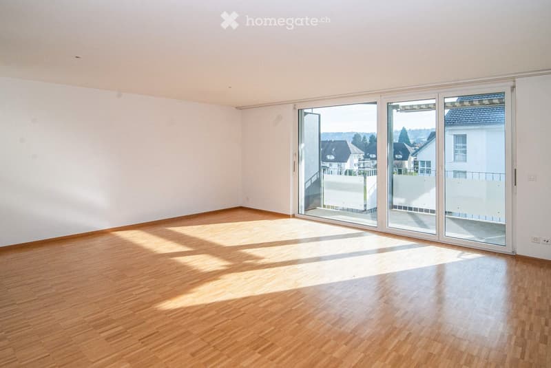 Empty room with wooden flooring and large sliding glass doors leading to a balcony or terrace. The walls are white, and the space is well-lit with natural light.