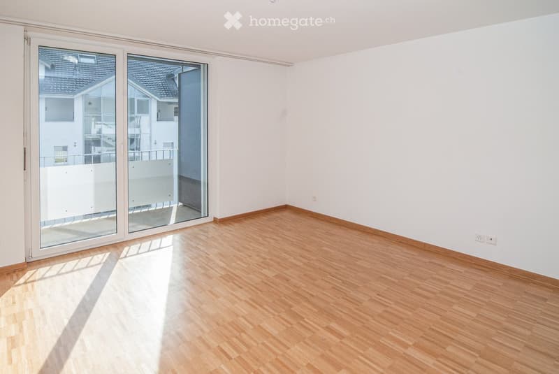 Empty room with wooden flooring, white walls, and large sliding glass doors leading to a balcony.