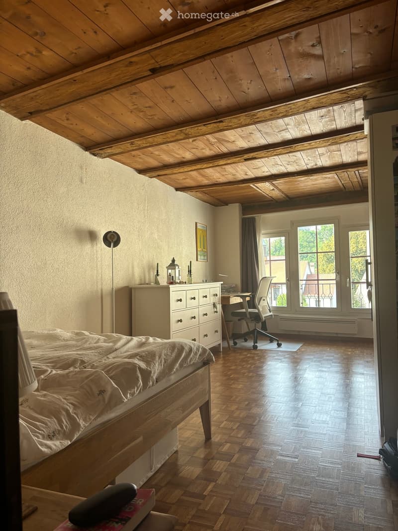 Cozy attic bedroom with wooden slanted ceilings, hardwood floors, a bed, a desk with a chair, a drawer unit, and a lamp.