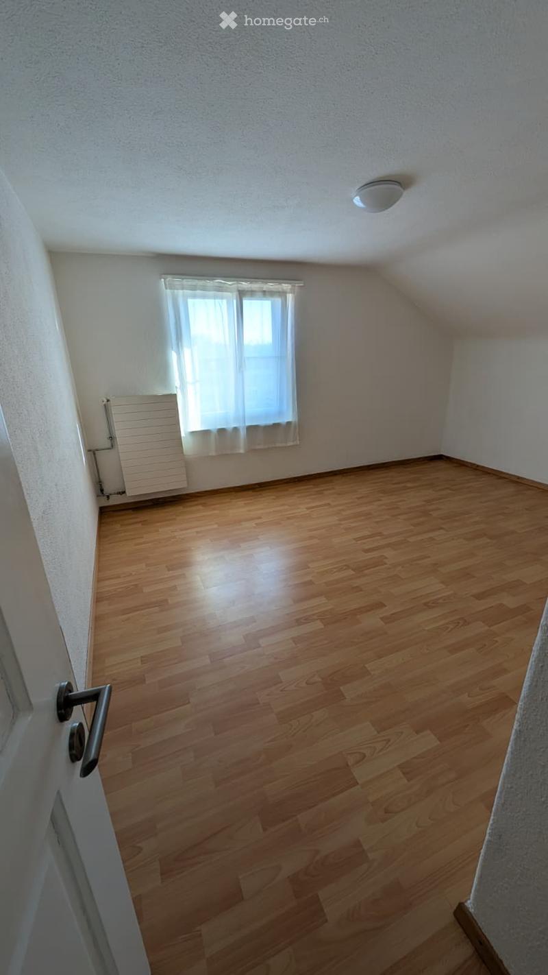 Empty room with wooden flooring, white walls, a window with white curtains, and a radiator. No furniture or equipment is present.