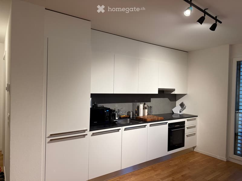 Modern kitchen with white cabinets, black countertops, stainless steel appliances, and wooden flooring.