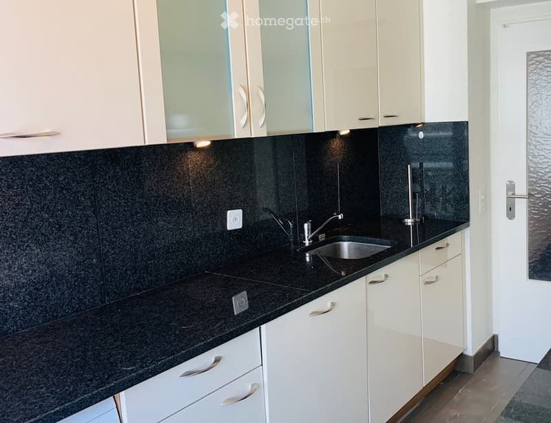 Modern kitchen with white cabinets, black granite countertops, and a stainless steel sink.