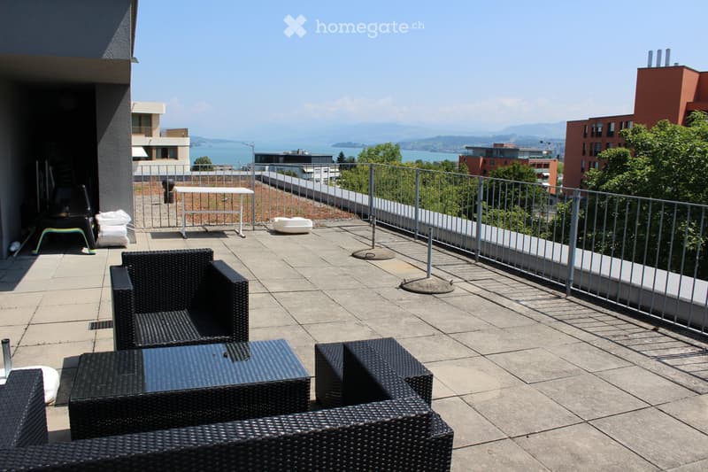 Balcony with wicker furniture, a table, and a view of the lake and mountains.