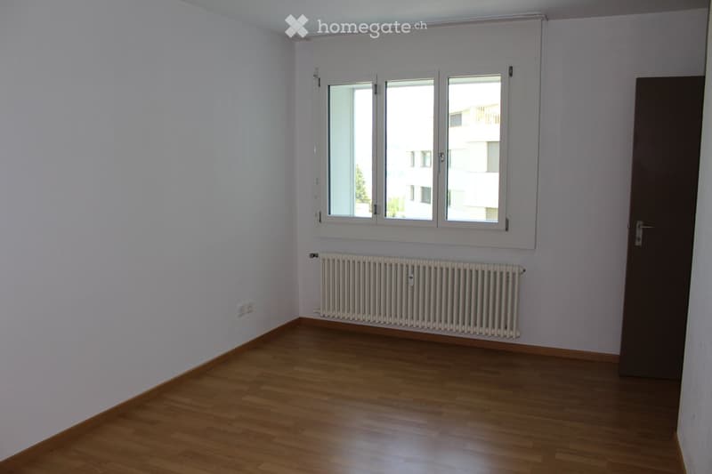 Empty room with wooden flooring, white walls, a radiator, and a large window with white frame. No furniture or equipment present.