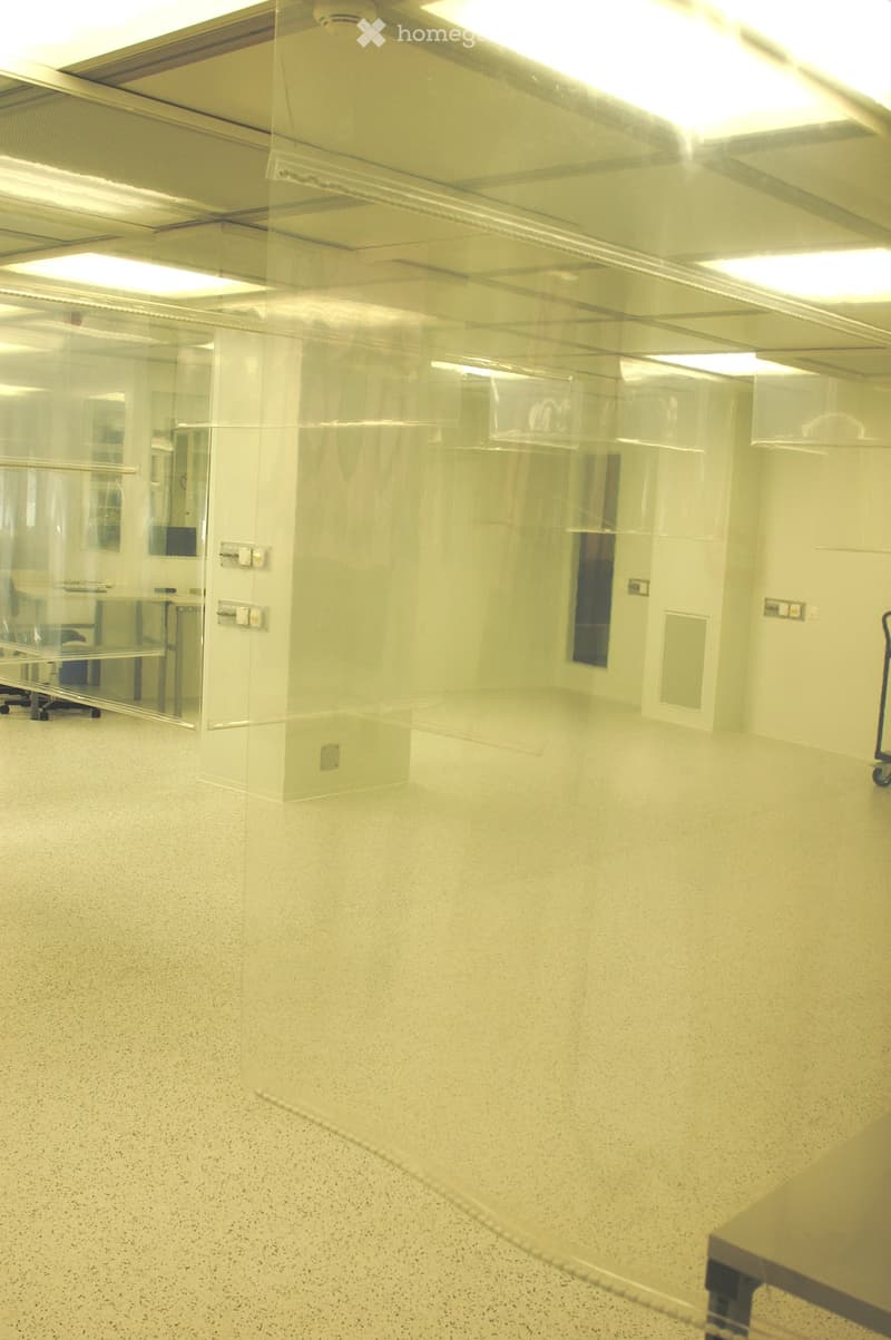 Empty room with white walls, a glass partition, and a speckled floor. No furniture or equipment is visible.