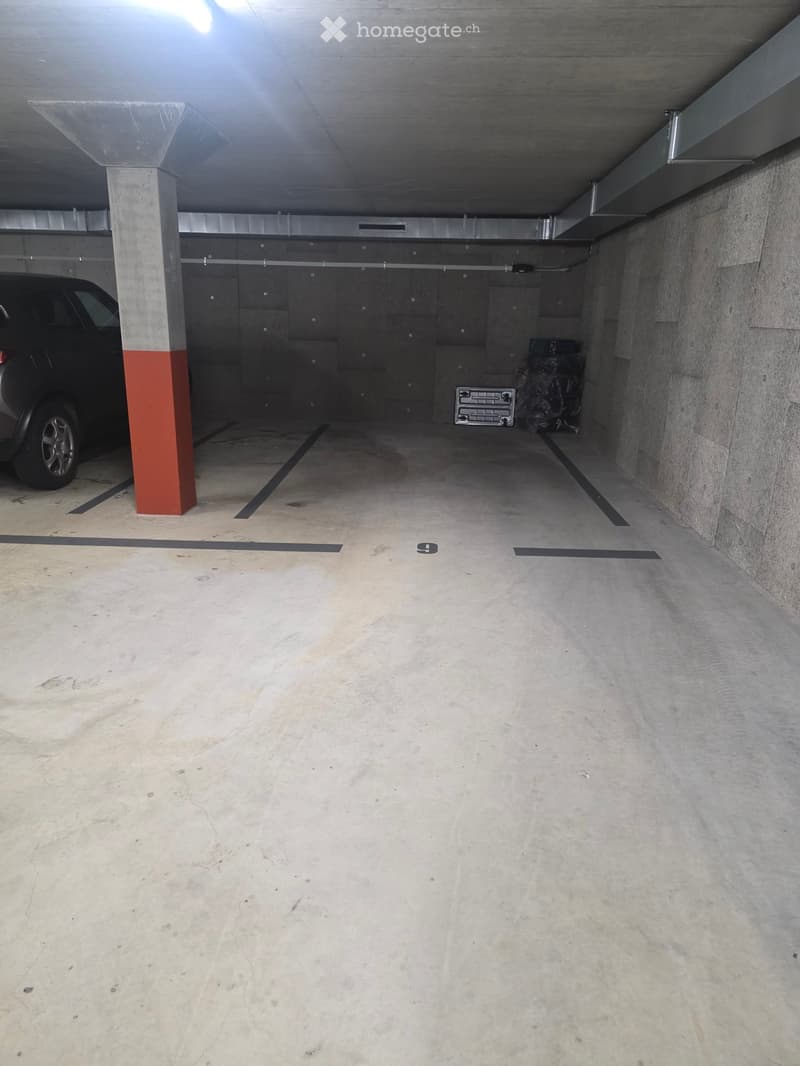 Underground parking area with concrete floors and walls, marked parking spaces, and a single parked car visible.