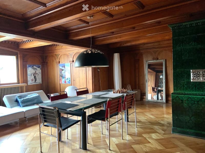 Elegant living and dining area with wooden beams, a large glass dining table, modern chairs, a white sectional sofa, and a large pendant lamp.