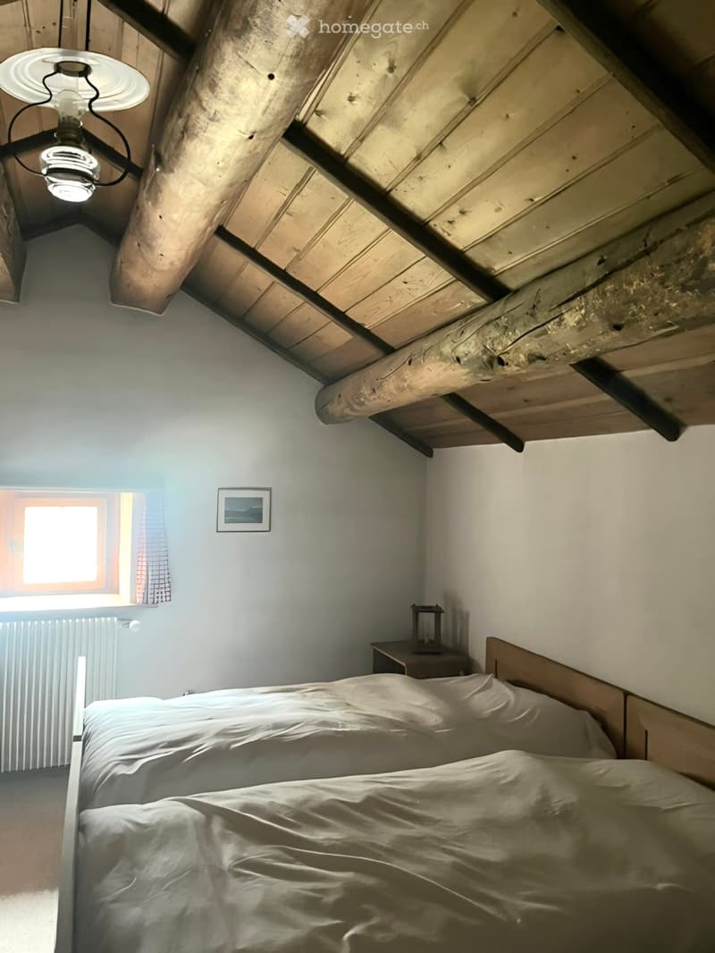 Cozy bedroom with a wooden slanted ceiling, a single bed with white bedding, a nightstand with a lamp, and a small picture frame on the wall.