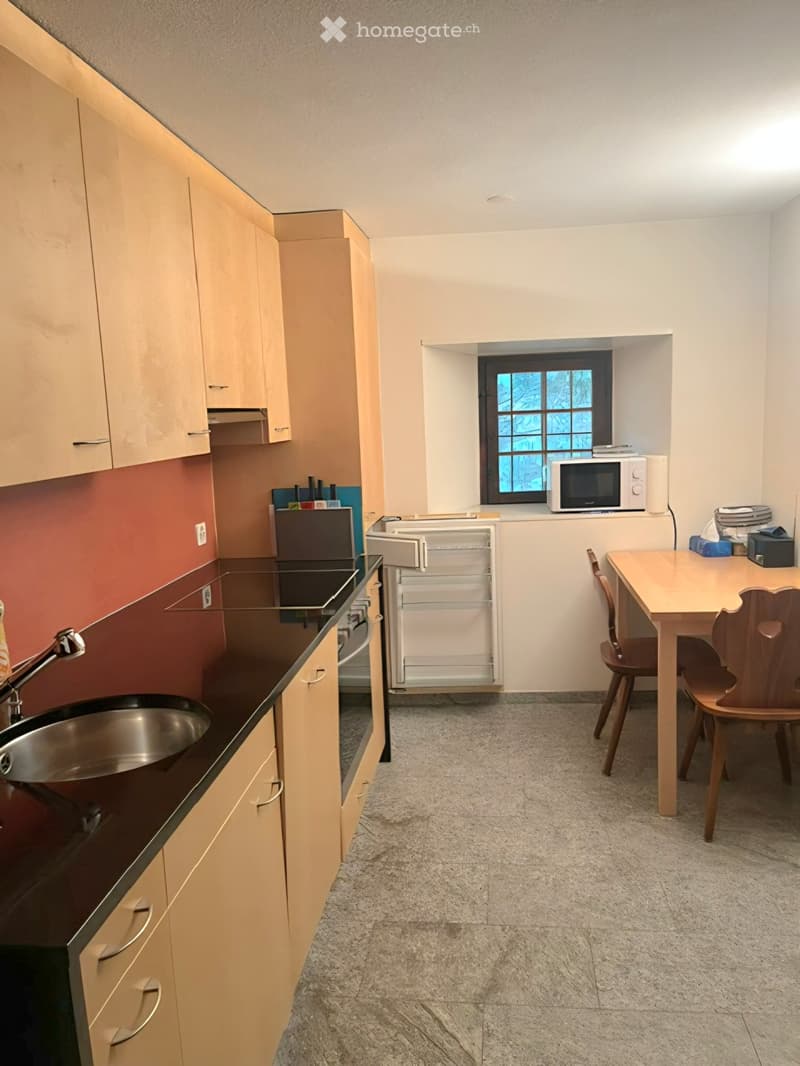 Modern kitchen with light wood cabinets, dark countertops, a sink, microwave, and a small dining area with a table and chairs.
