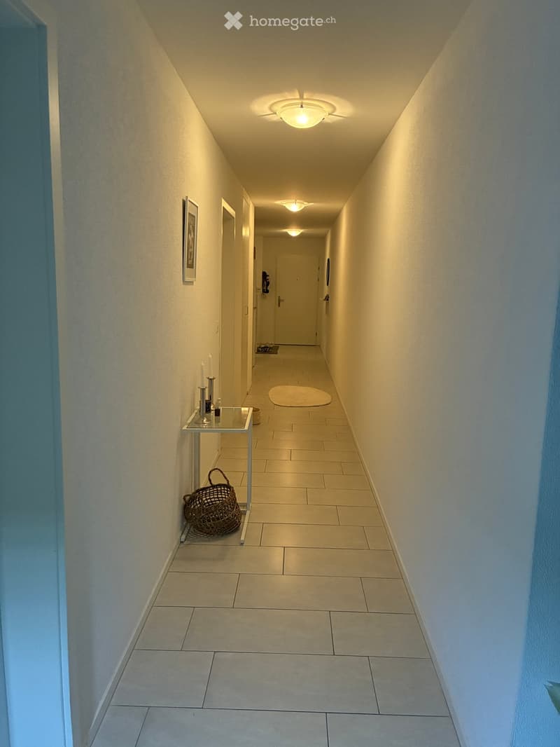 Clean hallway with tiled flooring, white walls, recessed lighting, and a small table with a basket and candles on one side.