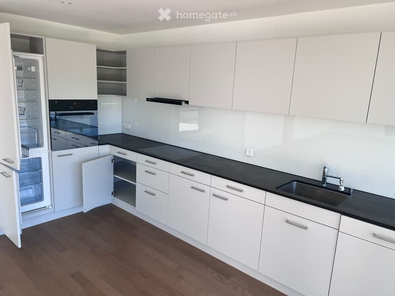 Modern kitchen with white cabinets, black countertops, and stainless steel appliances including a refrigerator, oven, and sink.