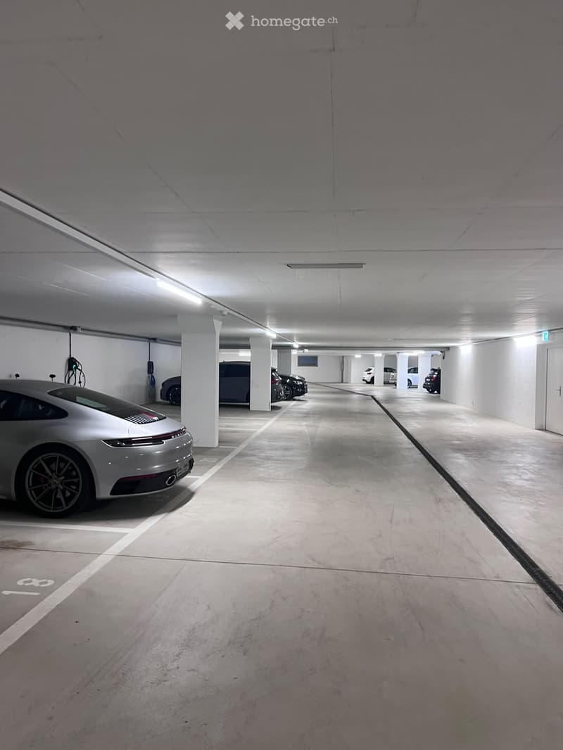Underground parking area with several parked cars, white pillars, and charging stations visible.