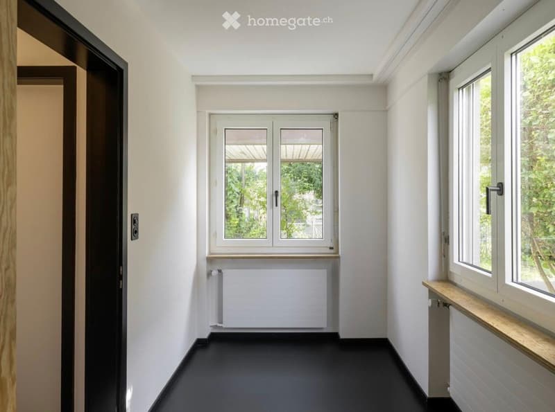Empty hallway with white walls, black floor, and large windows with wooden sills. No furniture or equipment present.
